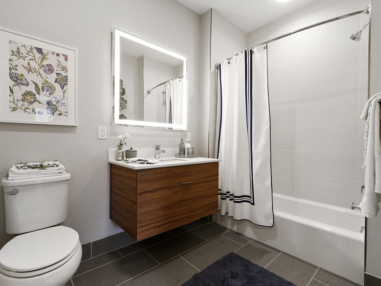 Large modern bathroom with light up mirror over sink and vanity and tiled flooring